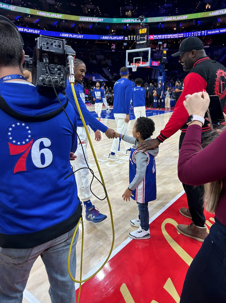 Youth shaking hands with 76ers player courtside